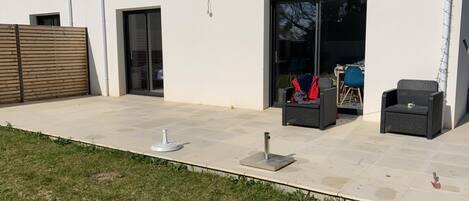 Un patio con suelo de baldosas, mobiliario exterior y una puerta corrediza de vidrio que da a un espacio interior.