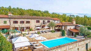 Edificio de piedra con piscina, mobiliario exterior y un paisaje boscoso de fondo.