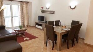 A living room with a sofa, a dining table set for four, a TV, and a small plant. - Clube Alvor Ria -Luxury 2 bedroom apartment with stunning views over the harbour (Alvor)