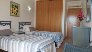 A bedroom with two beds, a wooden wardrobe, a nightstand, a vase with flowers, and a mirror. - Clube Alvor Ria -Luxury 2 bedroom apartment with stunning views over the harbour (Alvor)