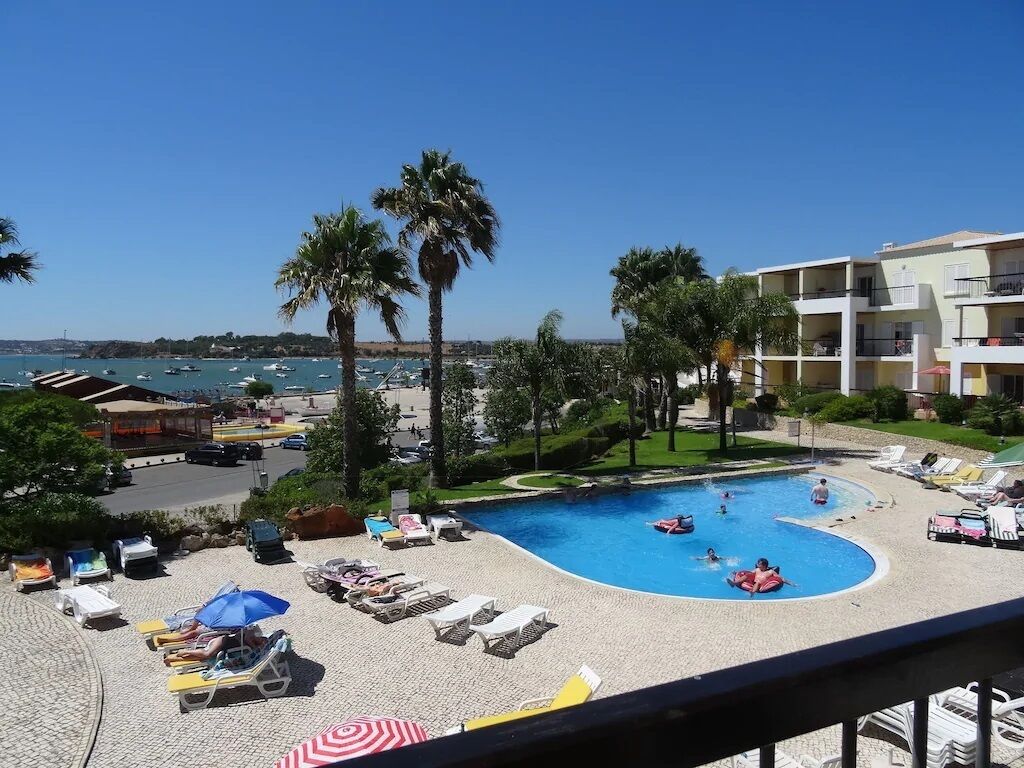 Ein Poolbereich mit Liegestühlen und Sonnenschirmen, umgeben von Palmen und Blick auf das Meer.