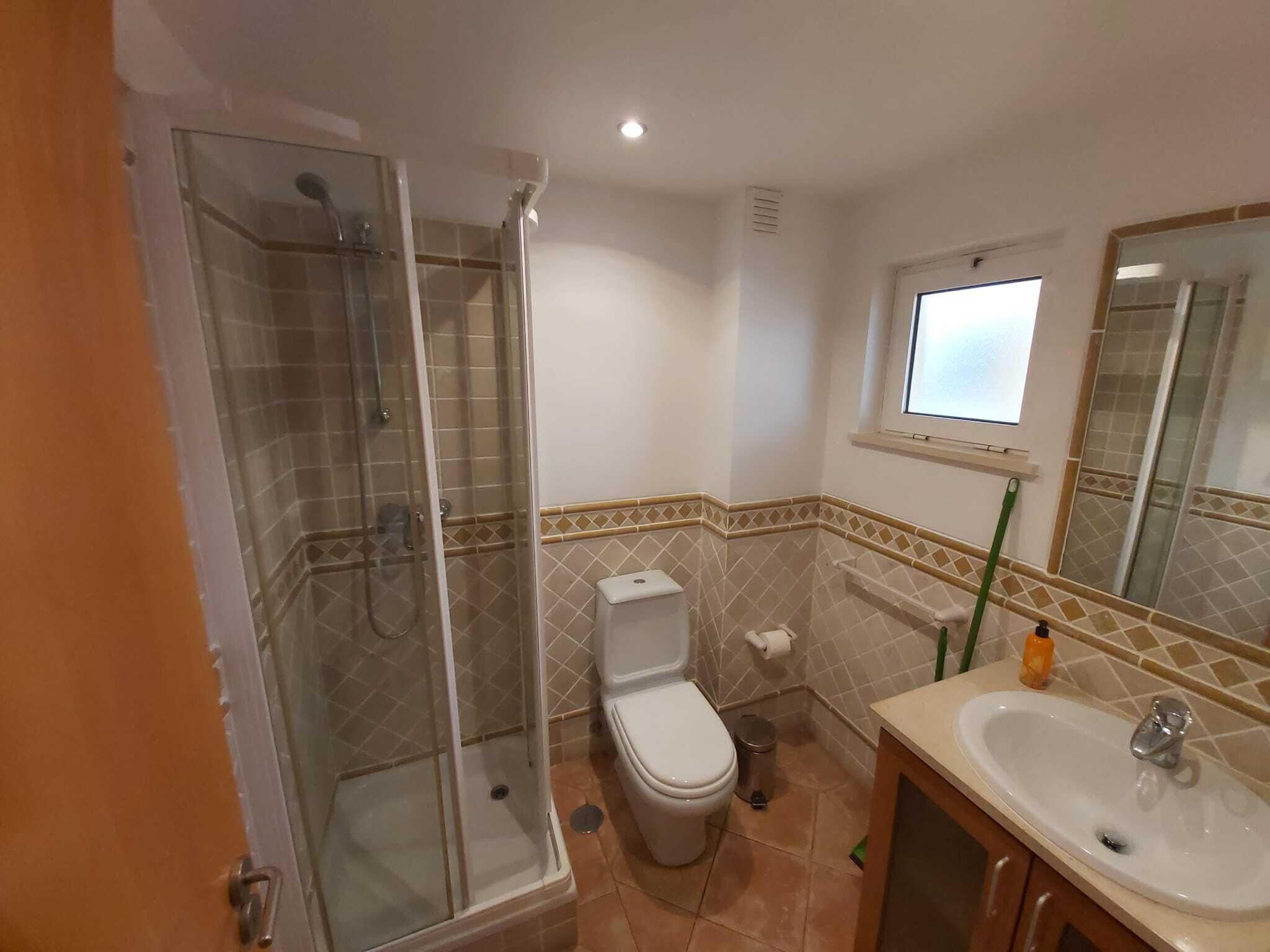 A bathroom with a glass-enclosed shower, a toilet, a sink, and a window.