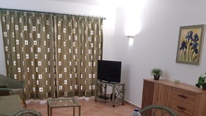 Olohuone, jossa on televisio, lasipöytä, tuoleja, sohva, kaappi ja seinällä taulu.