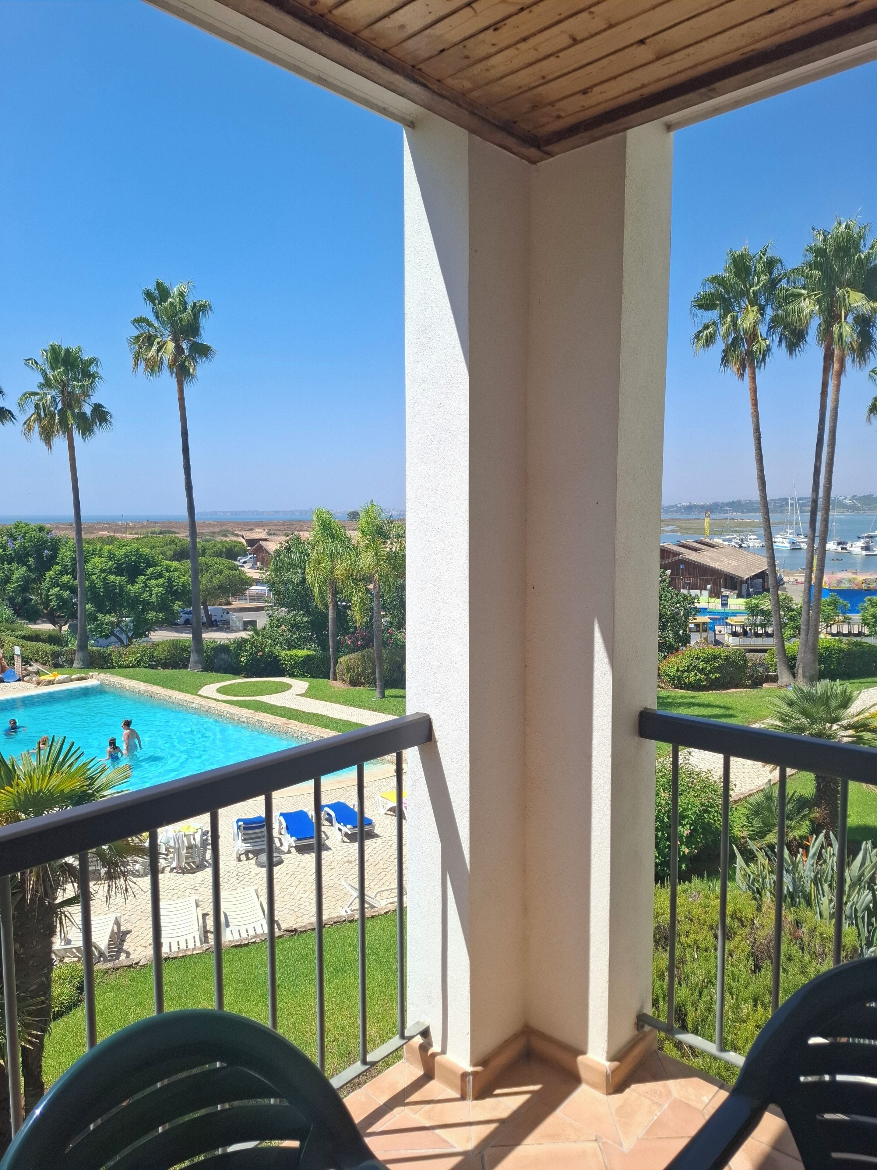 Een balkon met uitzicht op een zwembad, palmbomen en een jachthaven.