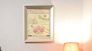 Et indrammet, gammelt reklameplakat på en væg, et bord med en stol og en lampe.