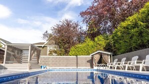 En swimmingpool med en klar blå vandoverflade, omgivet af hvide liggestole og et overdækket siddeområde.