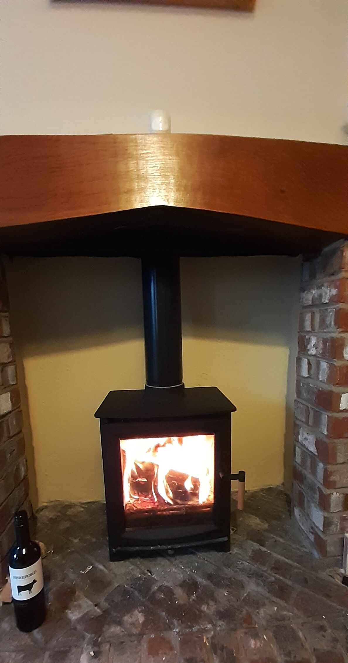 Ein Kaminofen mit sichtbarem Feuer, eine Ziegelwand und eine Flasche auf dem Boden.