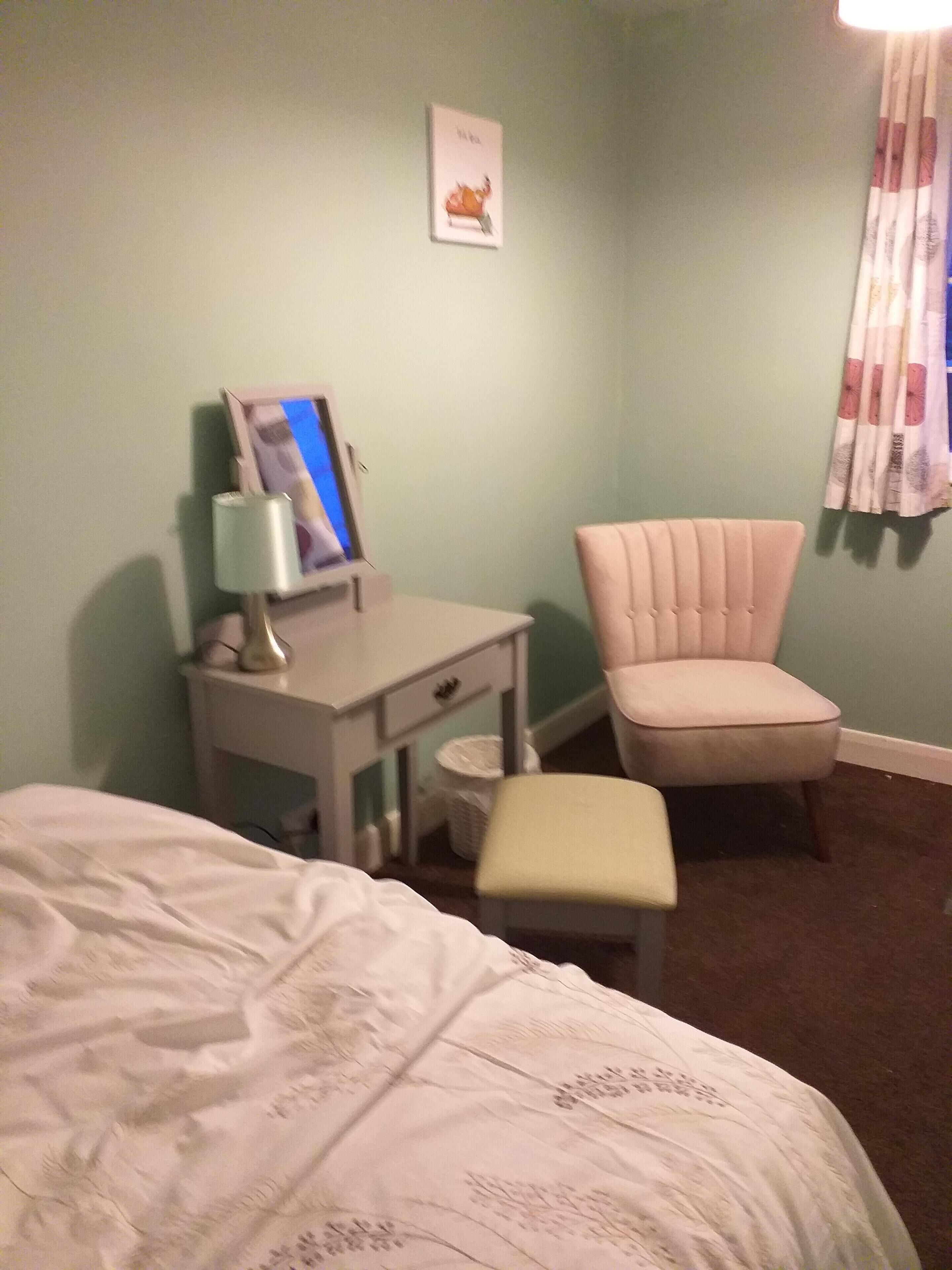 Una camera da letto con un letto, una scrivania con una lampada, una sedia e uno sgabello.