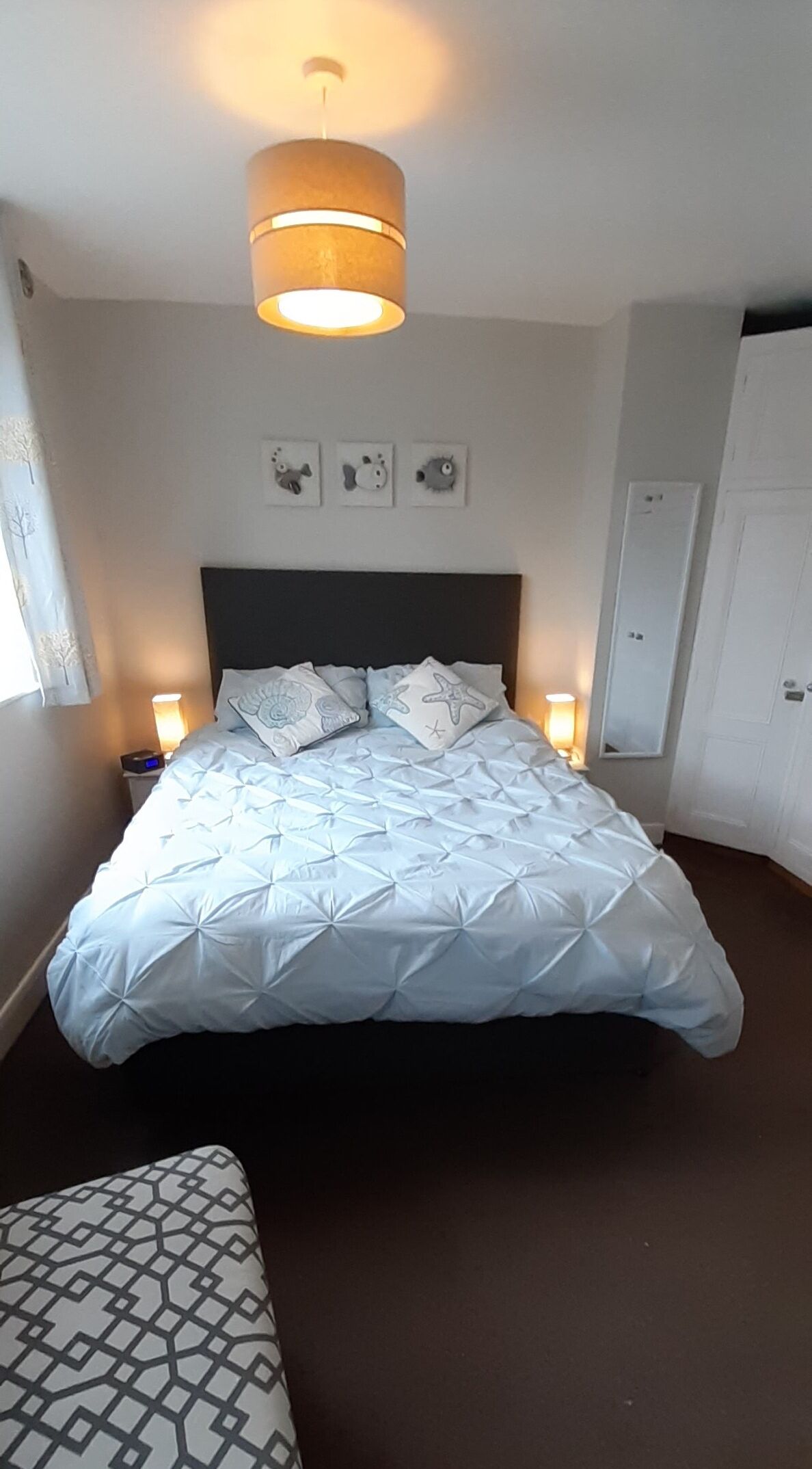 Uma cama bem arrumada com colcha estampada, uma luminária de cabeceira e um relógio de parede.