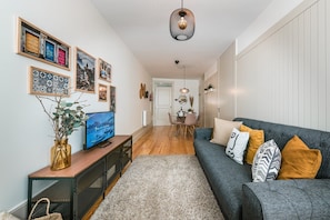 Una sala de estar moderna con un sofá gris, un televisor y un comedor al fondo.
