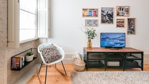 A cozy living room with a TV, a chair, a bookshelf, and a window with curtains. - GuestReady - Oporto Temptation Apartment (Porto)