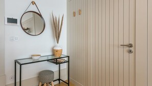 A minimalist room with a glass console table, a small stool, a mirror, a vase with pampas grass, and a wardrobe with vertical lines. - GuestReady - Oporto Temptation Apartment (Porto)