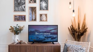 Un saló amb televisió de pantalla plana que mostra una vista panoràmica, una taula de consola de fusta amb un ram de plantes, una cadira de vímet i obra d'art penjada a la paret.