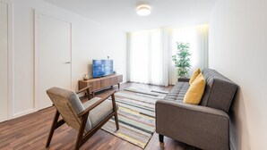 Un salon moderne comprenant un canapé, un fauteuil, un meuble de rangement en bois et un téléviseur.