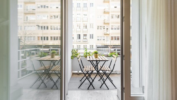 Un balcon avec une table et des chaises en bois, des plantes en pot et une vue sur des immeubles d’habitation.