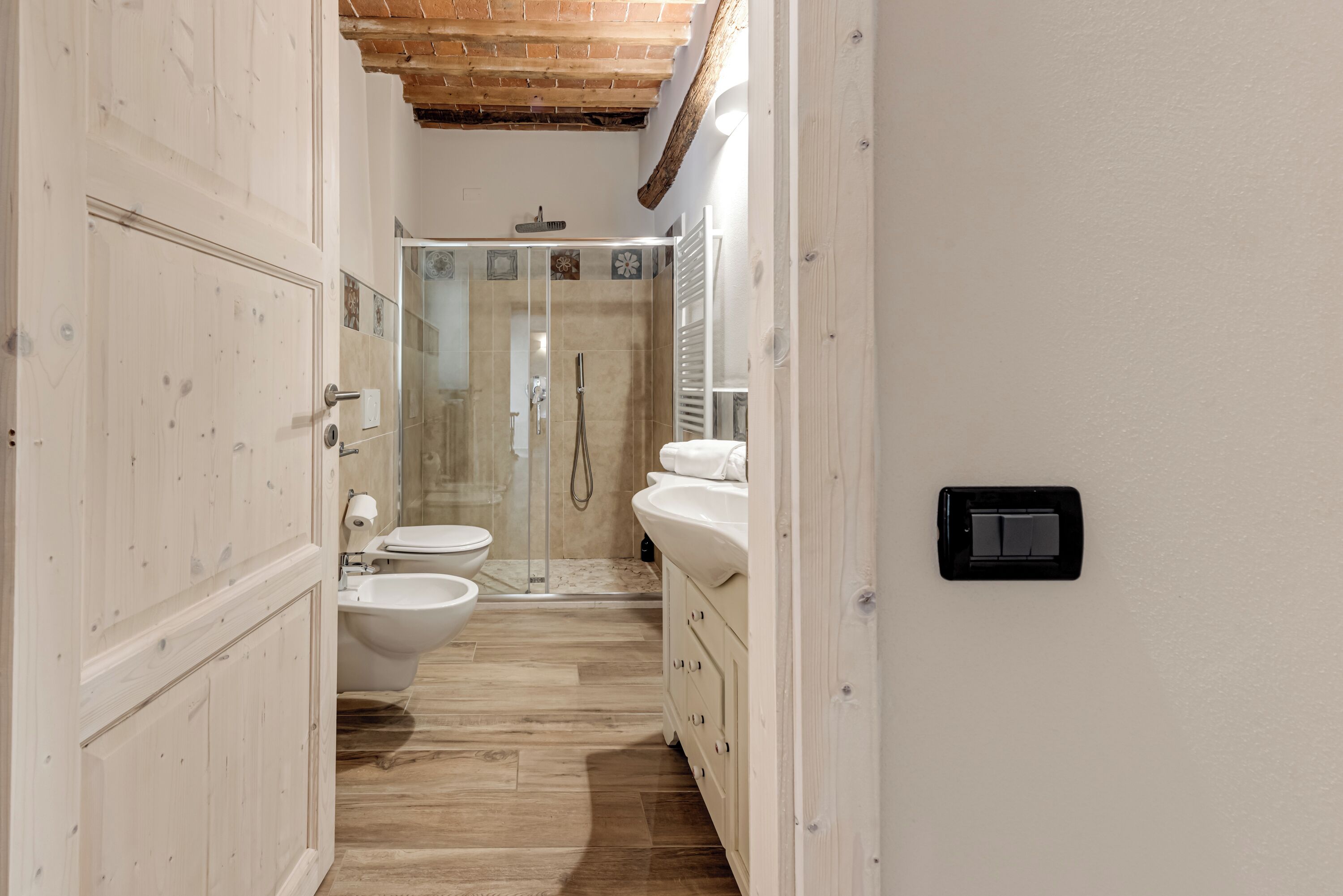 A narrow bathroom with a shower, toilet, bidet, and vanity.