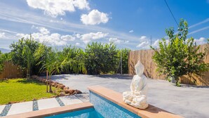Ein Schwimmbecken mit Buddha-Statue, umgeben von einem Holzzaun und viel Grün.