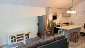 A modern kitchen with a stainless steel refrigerator, a microwave, and a built-in oven. There is a small island with a sink and stools. - Track and seasonal rental (Saratoga Springs)