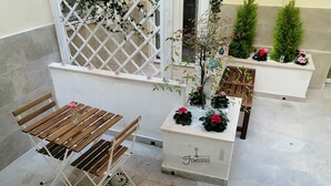 A patio area with a wooden bench, a small table with a vase of flowers, and a planter box with plants and flowers. - Dimora Fantasia Charme B&B (Bari)