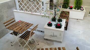 Una zona patio con una panca di legno, un tavolino con un vaso di fiori e un fioriera con piante e fiori.