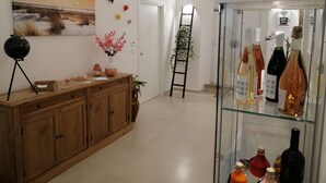 A hotel lobby with a wooden cabinet, a glass display case with bottles, a painting on the wall, and a ladder with plants. - Dimora Fantasia Charme B&B (Bari)
