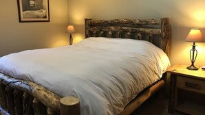 Een bed met een houten hoofdeinde, twee bedlampen en een ingelijste foto aan de muur.