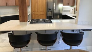 Een moderne keuken met een centraal eiland, roestvrijstalen apparatuur en zwarte barkrukken.