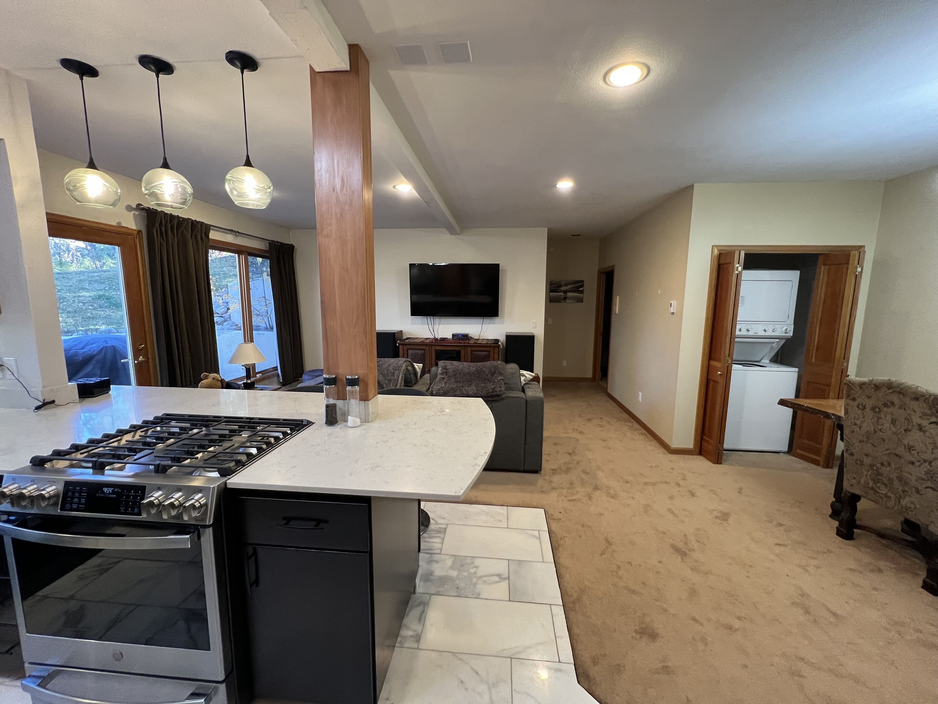 Una cocina moderna con estufa, horno y lavavajillas integrados, un comedor con una isla grande, y una sala de estar con sofá y televisor.