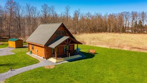 A log cabin with a porch, a small shed, and a grassy field.