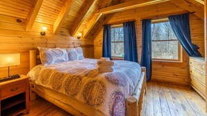 A wooden cabin bedroom with a bed, a nightstand, and a window with curtains.