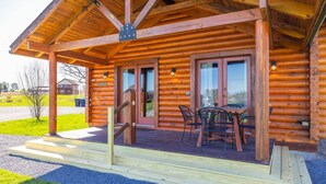 A wooden log cabin with a covered porch, a dining table, and chairs.