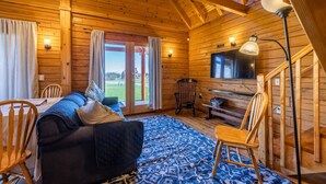 A cozy log cabin interior with a sofa, chairs, a TV, and a staircase.