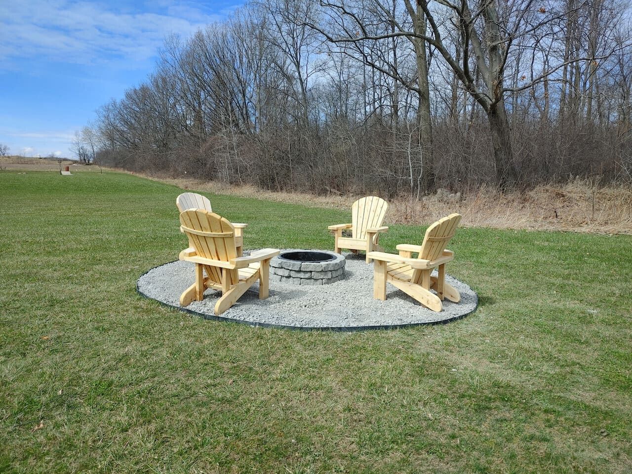 Un espacio de estar al aire libre con forma circular, con cuatro sillas Adirondack alrededor de un hogar de piedra.