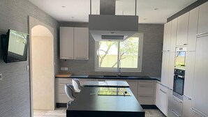 A modern kitchen with a central island, built-in appliances, and a large window providing natural light. - Luxurious villa in cap d'agde  (Agde)