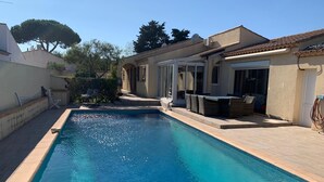 A rectangular swimming pool with a tiled deck, surrounded by a covered patio area with outdoor furniture. - Luxurious villa in cap d'agde  (Agde)