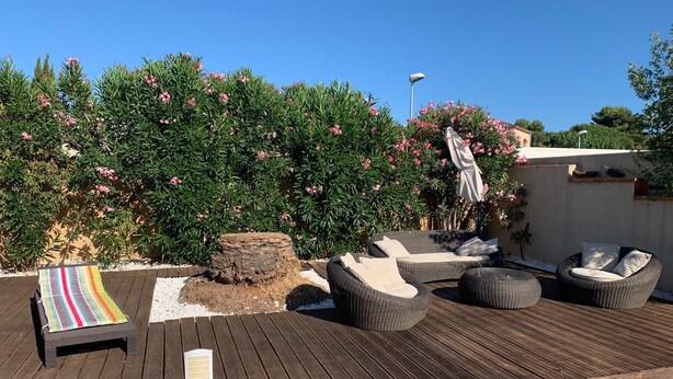 A wooden deck with outdoor furniture, including a sofa and chairs, surrounded by lush greenery and flowering plants. - Luxurious villa in cap d'agde  (Agde)