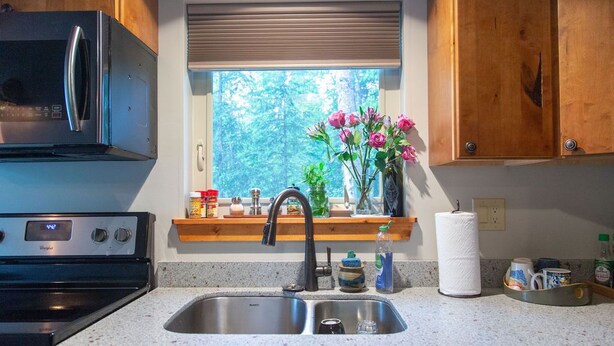 A kitchen with a stainless steel sink, a microwave, and wooden cabinets. - Aviator Cabin (Talkeetna)