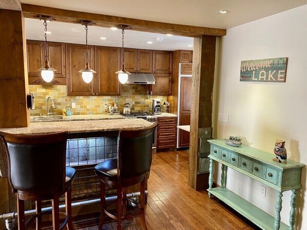Una cocina con armarios de madera, una zona de bar con taburetes, una mesa consola de estilo vintage y un cartel que dice 'Welcome to the Lake'.