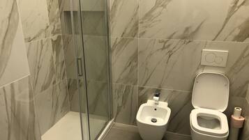 Un baño moderno con cabina de ducha de cristal, un bidé y un inodoro.