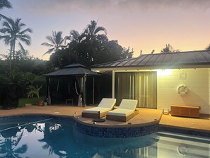 A swimming pool with lounge chairs, a covered seating area, and a building with a lifebuoy. - Kona Keauhou Newly Remodeled Home, Quiet private home on Golf course with
Pool. (Kailua-Kona)