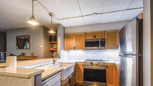 Une cuisine compacte dotée de meubles en bois, d’appareils électroménagers en acier inoxydable, d’un four à micro-ondes, d’un lave-vaisselle et de luminaires suspendus.