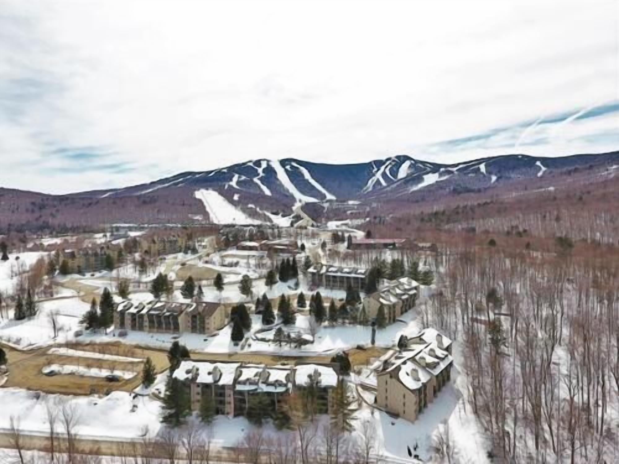 A snow-covered village with buildings clustered around a central square, surrounded by mountains.