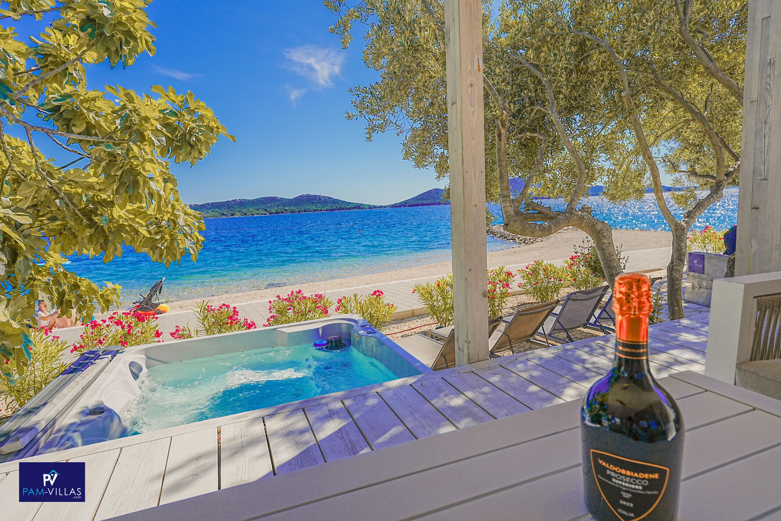 Una terrassa de fusta amb un bany d'hidromassatge, una ampolla de Prosecco Valdossiana i vista al mar i a la platja.