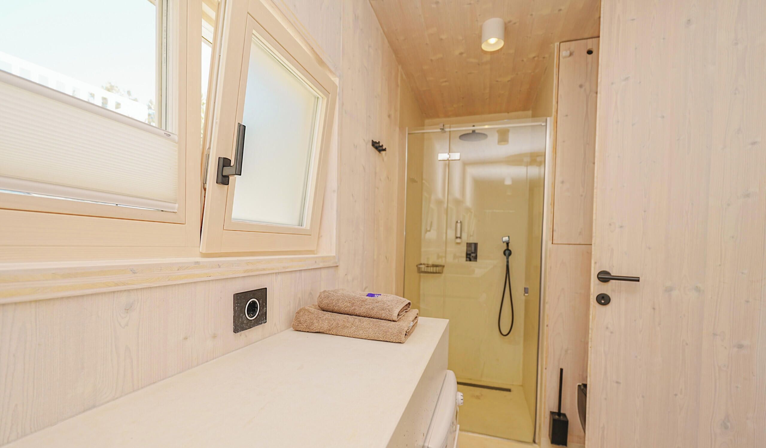 Une salle de bain avec une douche, une serviette posée sur le comptoir et une fenêtre avec des stores.