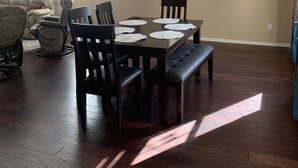 Un coin repas agrémenté d’un lustre, d’un canapé et d’une fenêtre avec des stores.