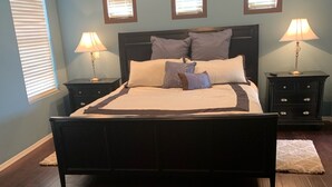 Une chambre à coucher avec un grand lit, deux tables de chevet et trois fenêtres fixées au mur.