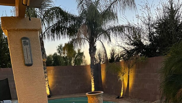 Un espace aménagé au bord de la piscine, avec un pilier en pierre, un foyer et une personne se relaxant sur une chaise.
