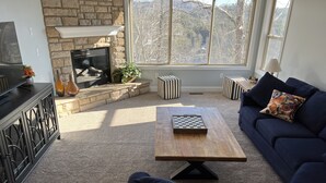Ein Wohnzimmer mit Kamin, einer Couch, einem Couchtisch und gestreiften Hocker.