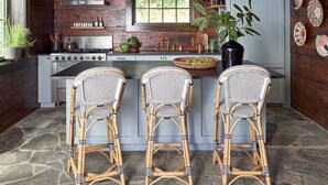 A rustic kitchen with a central island, three wicker bar stools, hanging pendant lights, and a stone floor. - The Kingfisher: Flat Mountain Farm (Highlands)