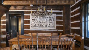 A rustic dining area with a wooden table and chairs, a chandelier with antlers, and a wall tapestry depicting wildlife. - The Kingfisher: Flat Mountain Farm (Highlands)